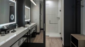 A modern bathroom with a large mirror, two sinks, and a walk-in shower.