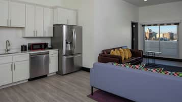 Una cocina moderna con electrodomésticos de acero inoxidable, una zona de comedor con sofá y cojines, y vistas a la ciudad a través de un ventanal grande.