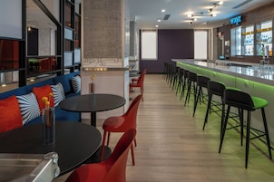 Un área de bar moderna con mostrador, taburetes y zona de estar con mesas y sillas.