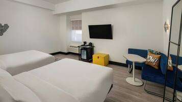 A hotel room with two beds, a TV, a small table, and a sofa.