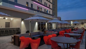 An outdoor seating area with tables and chairs, some with umbrellas, and a bar area with stools. - Aloft by Marriott Memphis Downtown (Memphis)