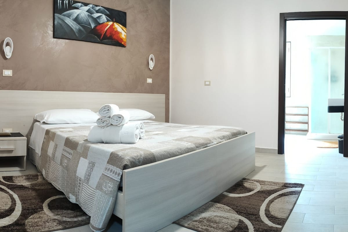 Une chambre d’hôtel moderne avec un grand lit, une table de chevet, un téléviseur fixé au mur et une vue sur l’extérieur.