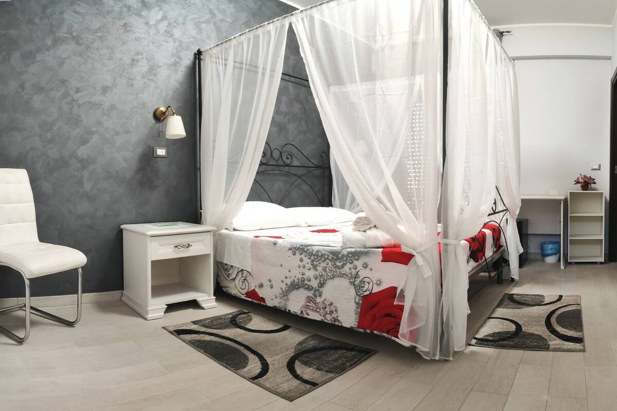 Une chambre à coucher avec un lit à baldaquin, une table de chevet, une chaise et une petite étagère.