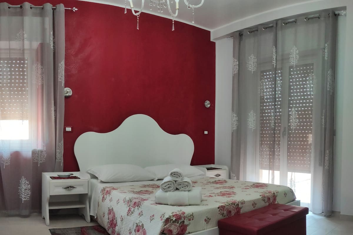 Une chambre à coucher avec un lit blanc, des murs d’une couleur rouge vive et un lustre.