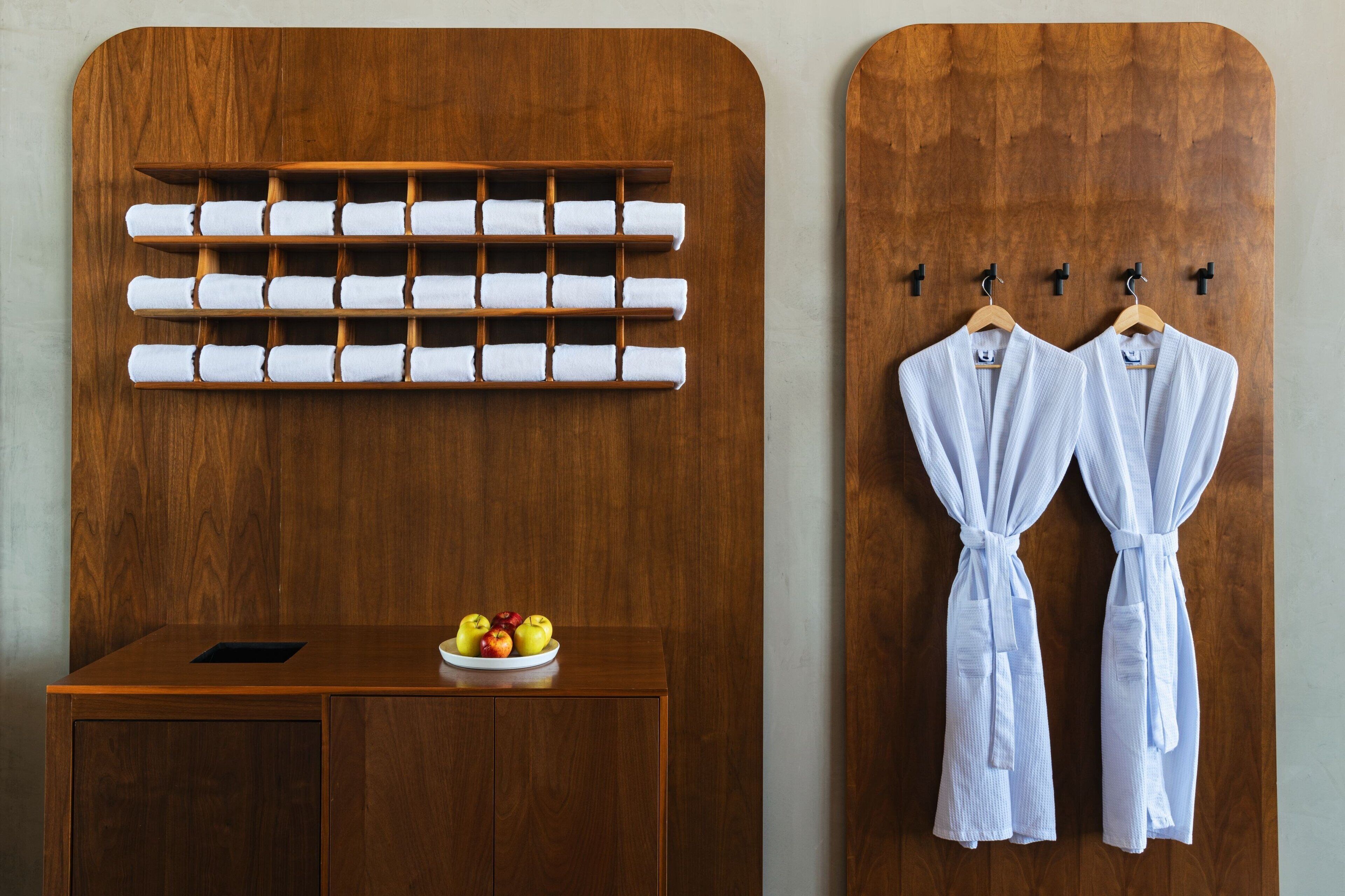 A wooden wall with a towel rack holding multiple towels and two robes hanging on hooks.