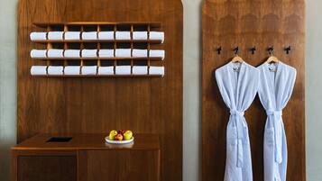 A wooden wall with a towel rack holding multiple towels and two robes hanging on hooks.
