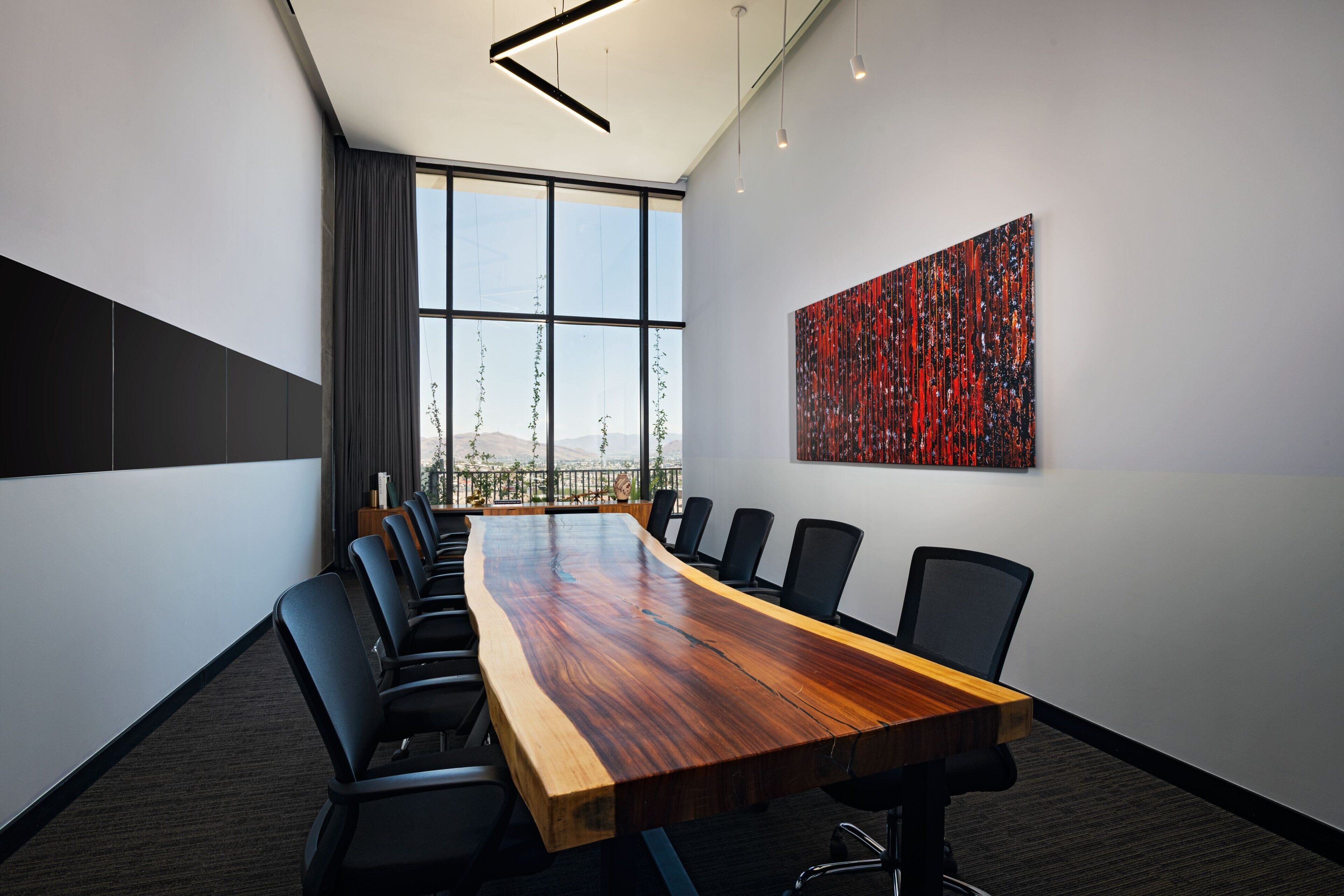 Une salle de conférence avec une longue table en bois, des chaises noires et un grand tableau abstrait accroché au mur.