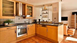 Eine moderne Küche mit Holzschränken, einem eingebauten Ofen, einer Kaffeemaschine und einem Regal mit Küchenutensilien.