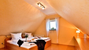 Ein gemütlicher, dreieckiger Raum mit einem Bett, einem kleinen Tisch mit einer Lampe und einem fenster mit Vorhängen.