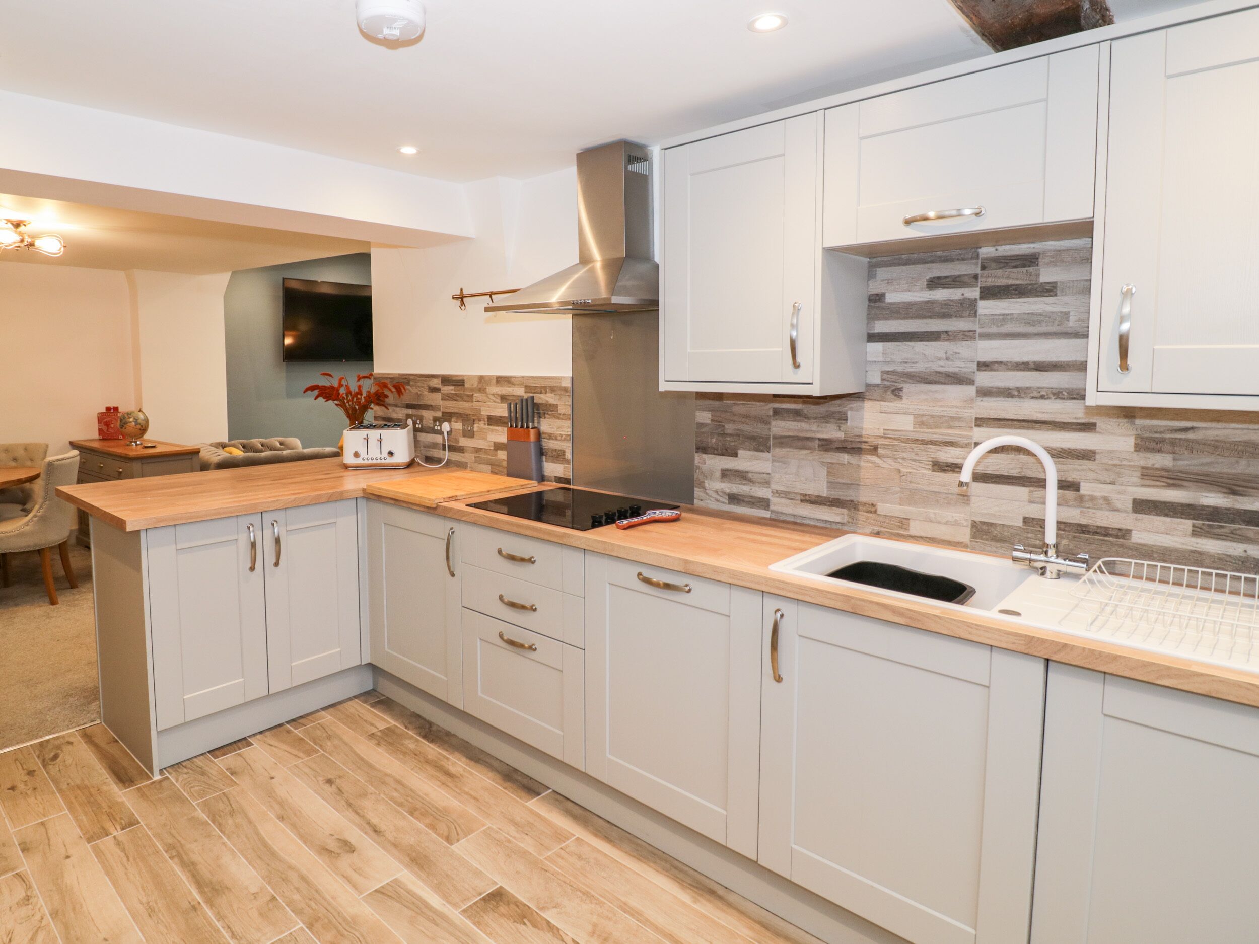 A modern kitchen with light-colored cabinets, a wooden countertop, a stainless steel range hood, and a tiled backsplash.