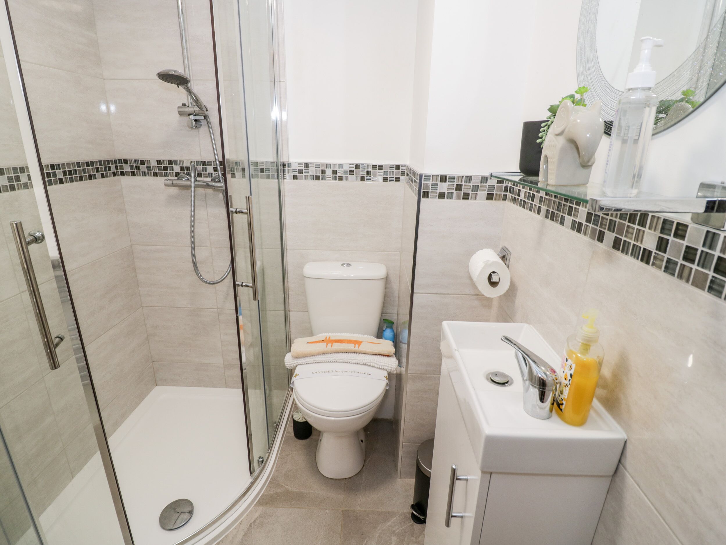 Un baño moderno con ducha envuelta en vidrio, inodoro y lavamanos con artículos de aseo.