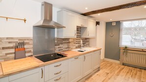 A modern kitchen with light grey cabinets, a wooden countertop, and a stainless steel range hood. - The Fox (Bridgnorth)