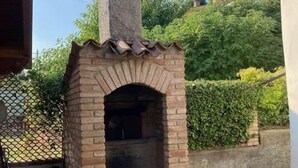 A brick-built outdoor oven with a chimney, surrounded by a tiled patio and a potted plant. - Casa Reale (Volta Mantovana)