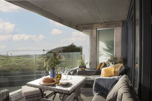 Ein Balkon mit Esstisch, Korbmöbeln und Blick aufs Meer.