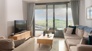 A modern living room with a large TV, comfortable seating, and a view of the countryside through large glass doors. - Ocean's Eleven, The Liner - Sea view - footsteps from the beach - Free parking (Falmouth)