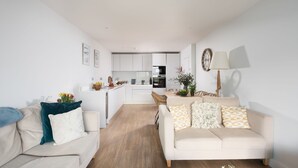 A modern living room with a sofa and a dining area, connected to a kitchen with white cabinets and a built-in oven. - Ocean's Eleven, The Liner - Sea view - footsteps from the beach - Free parking (Falmouth)