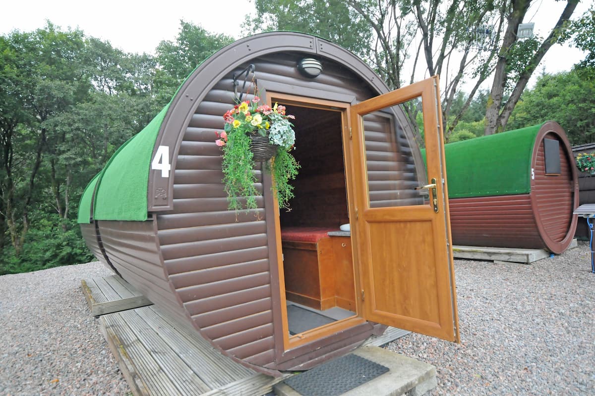 Une petite structure cylindrique en bois, dotée d’une porte ouverte, laissant apercevoir un banc à l’intérieur.