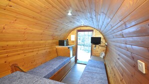 A cozy cabin interior with wooden walls, a bench, a small table, and a television. - Glamping Pods (Kinlochleven)