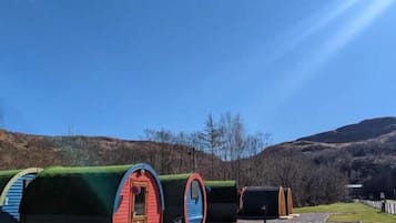 En rad cylindriska stugor med dörrar, placerade längs en grusgång, omgivna av gräs och kullar.