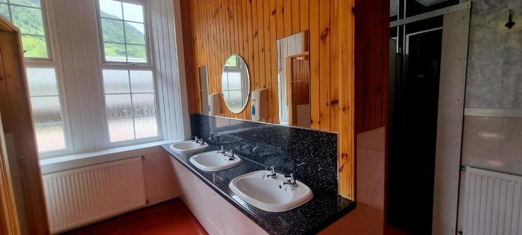 Baño con tres lavamanos, un espejo y paneles de madera.