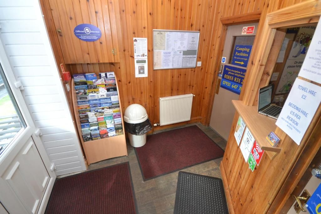 A small, wooden-facade room with a toilet, a waste bin, a notice board, and a small display of magazines.
