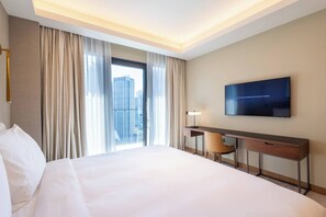 Habitación de hotel con una cama grande, un escritorio, una silla, un televisor y vistas a la ciudad desde la ventana.