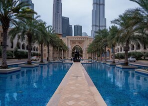 Zona de piscina con palmeras, un paseo central y un edificio con señalización 'EMAAR' al fondo.