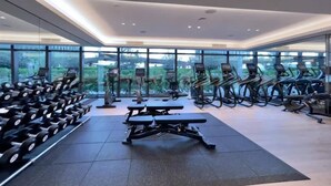 Une salle de sport moderne, équipée de matériel d’exercice, dotée de grandes fenêtres et offrant une vue sur la verdure.