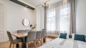 Une chambre d’hôtel moderne avec un grand lit, une table à manger avec des chaises, un lustre et une fenêtre avec des rideaux.