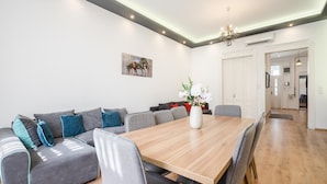 Un espace repas moderne avec une table en bois et des chaises à revêtement gris, un canapé gris agrémenté de coussins turquoise et un vase avec des fleurs.