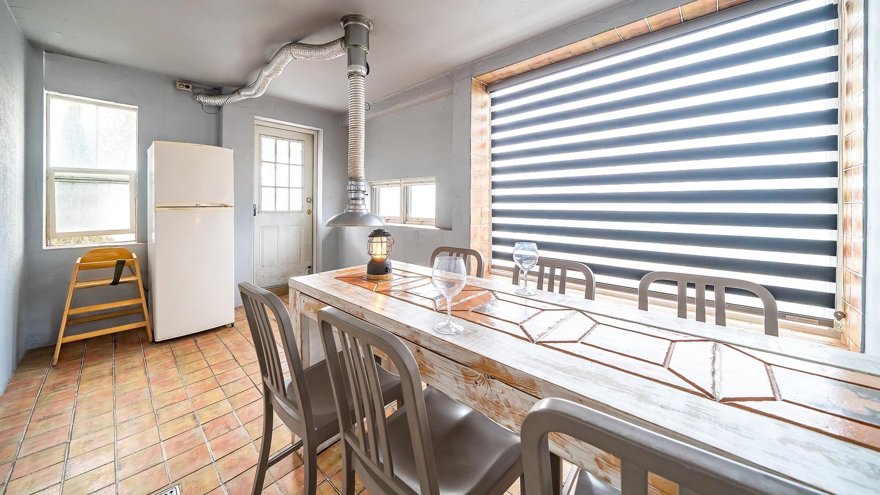 A kitchen with a wooden table, chairs, a refrigerator, a stove, and a window with blinds.
