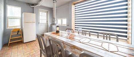 A kitchen with a wooden table, chairs, a refrigerator, a stove, and a window with blinds.