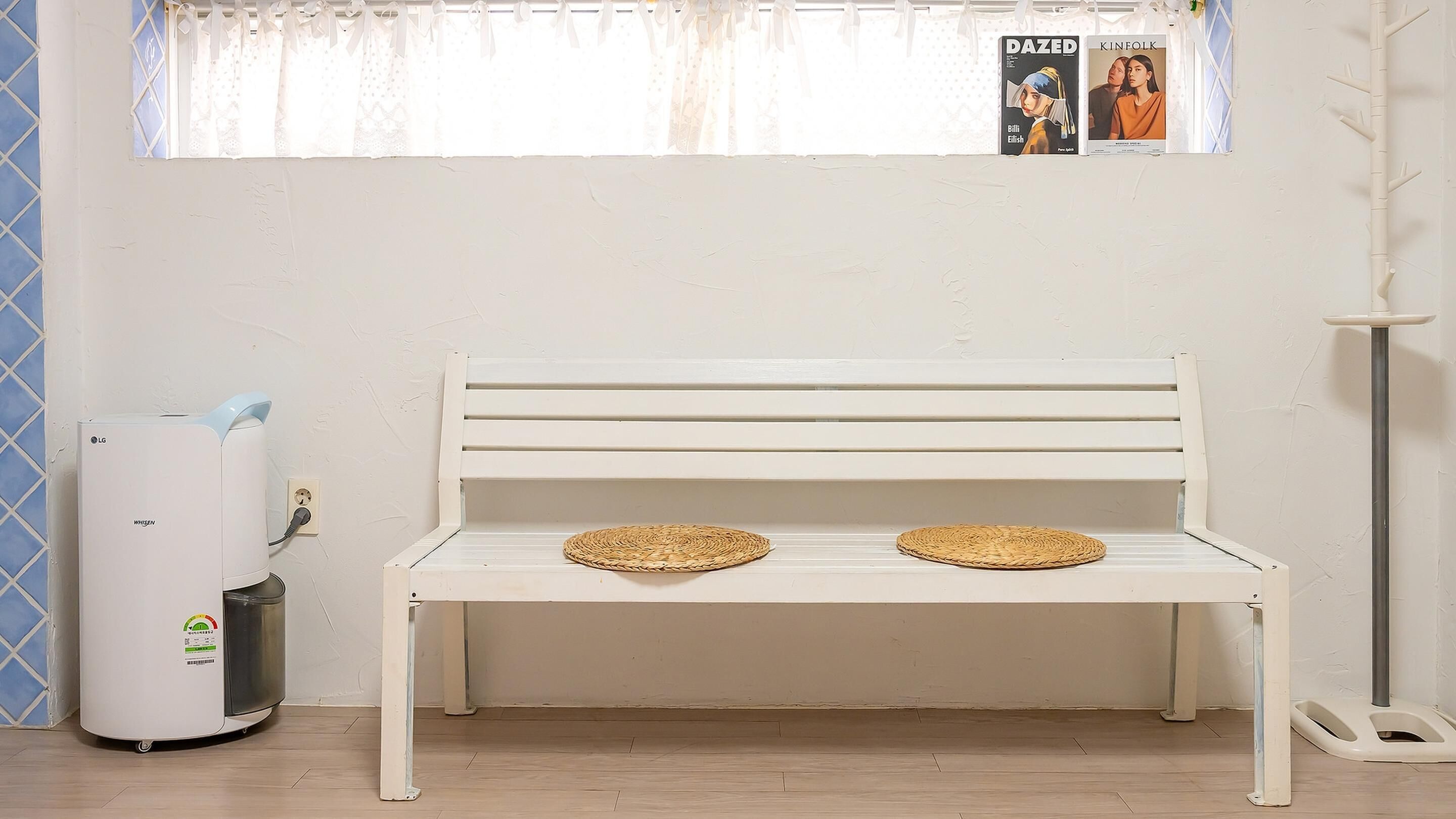 A white bench with woven placemats, a white radiator, and a window with a poster.