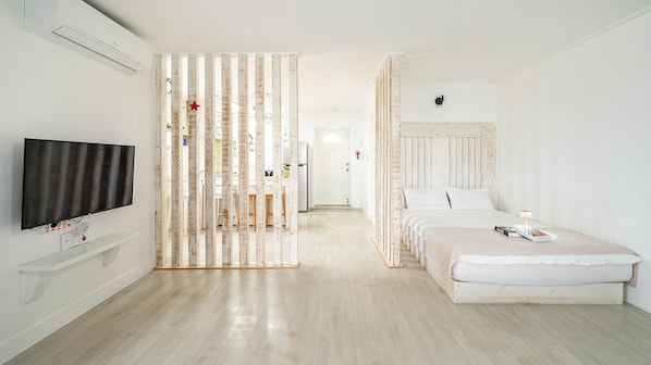 Habitación de hotel con piso de madera, cama con ropa blanca, televisor montado en la pared y separador de madera decorado con una estrella.