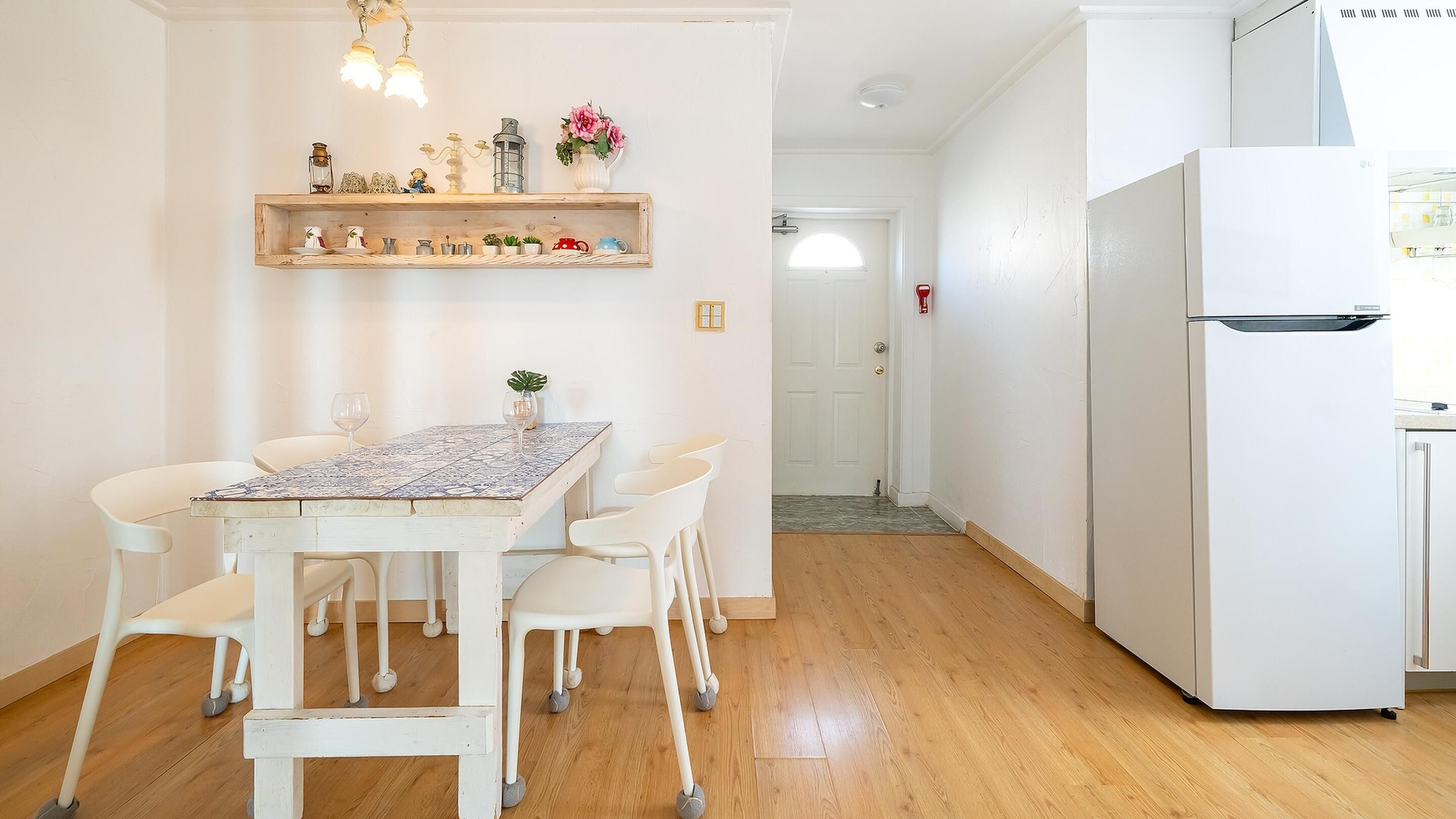 Un coin repas avec une table et des chaises, un réfrigérateur blanc et une étagère ornée d’objets décoratifs.