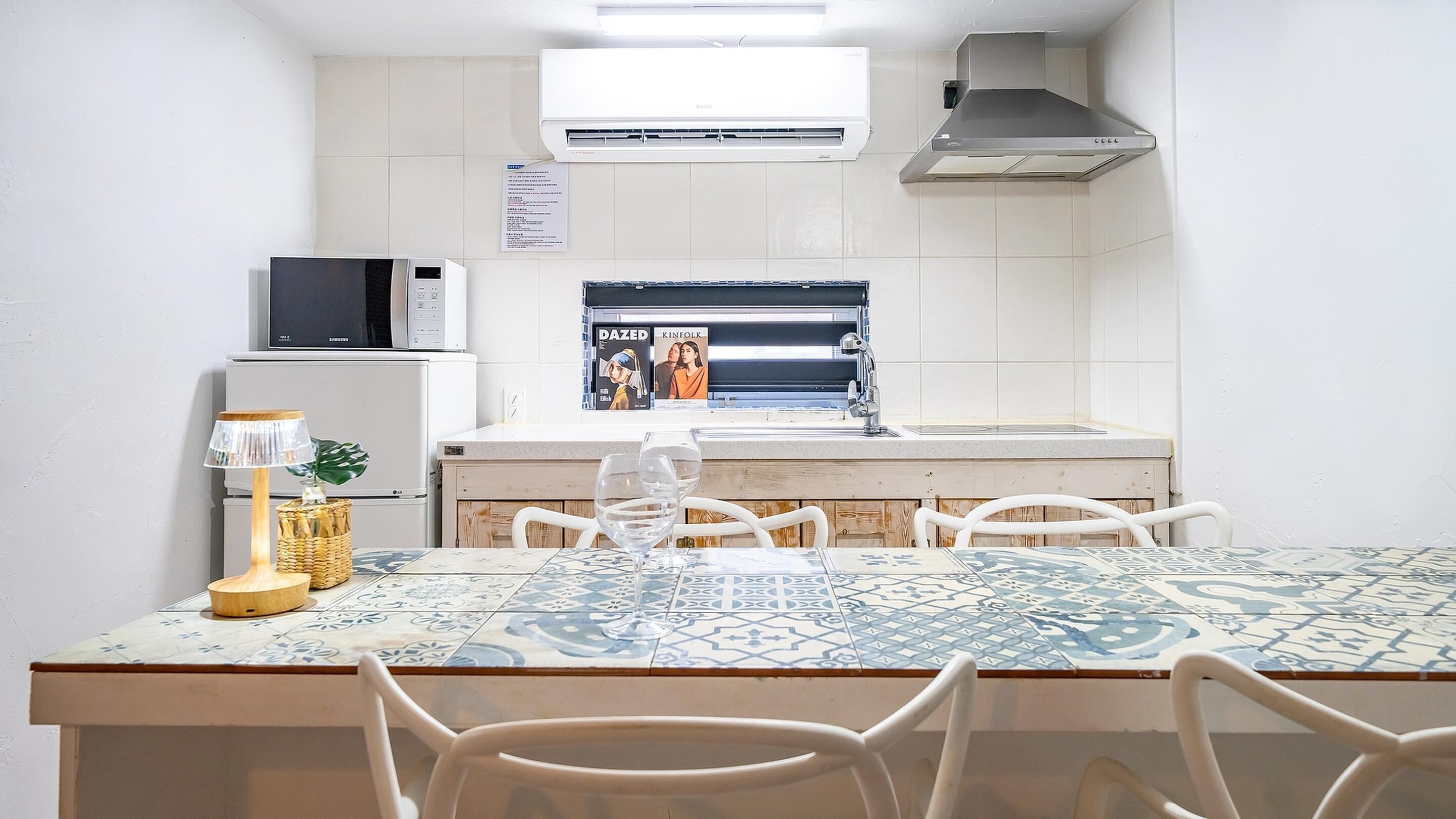 A compact kitchen with white tiles, a microwave, a coffee maker, and a sink.