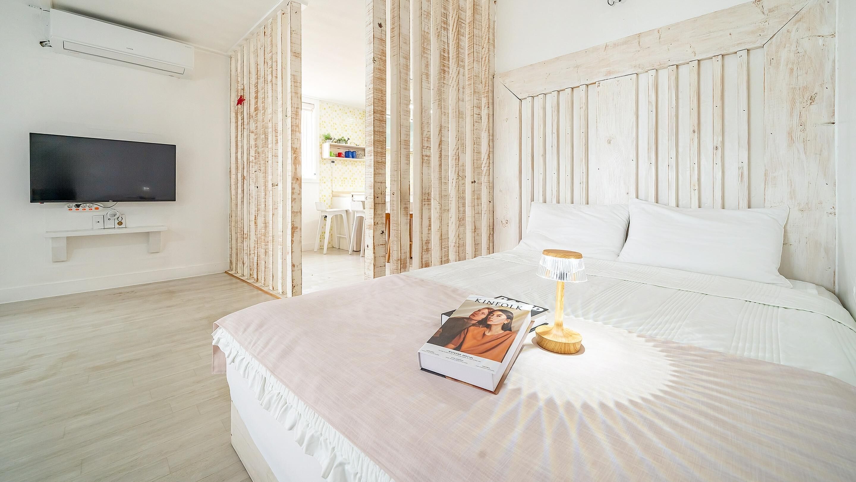 Ein Schlafzimmer mit einem Bett, einem Nachttisch mit Lampe, einem Wandfernseher und einem Bücherregal.