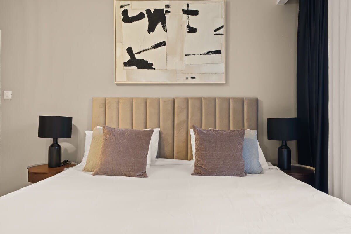 Una habitación de hotel con una cama grande, dos mesitas de noche con lámparas y una obra de arte abstracto colgada en la pared.