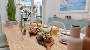 A breakfast table with various food items, a vase with flowers, and a painting on the wall. - Pool und Sauna mit Meerblick, Direkt an der Seebrücke - First Sellin Fewo 3.8 (Ostseebad Sellin)