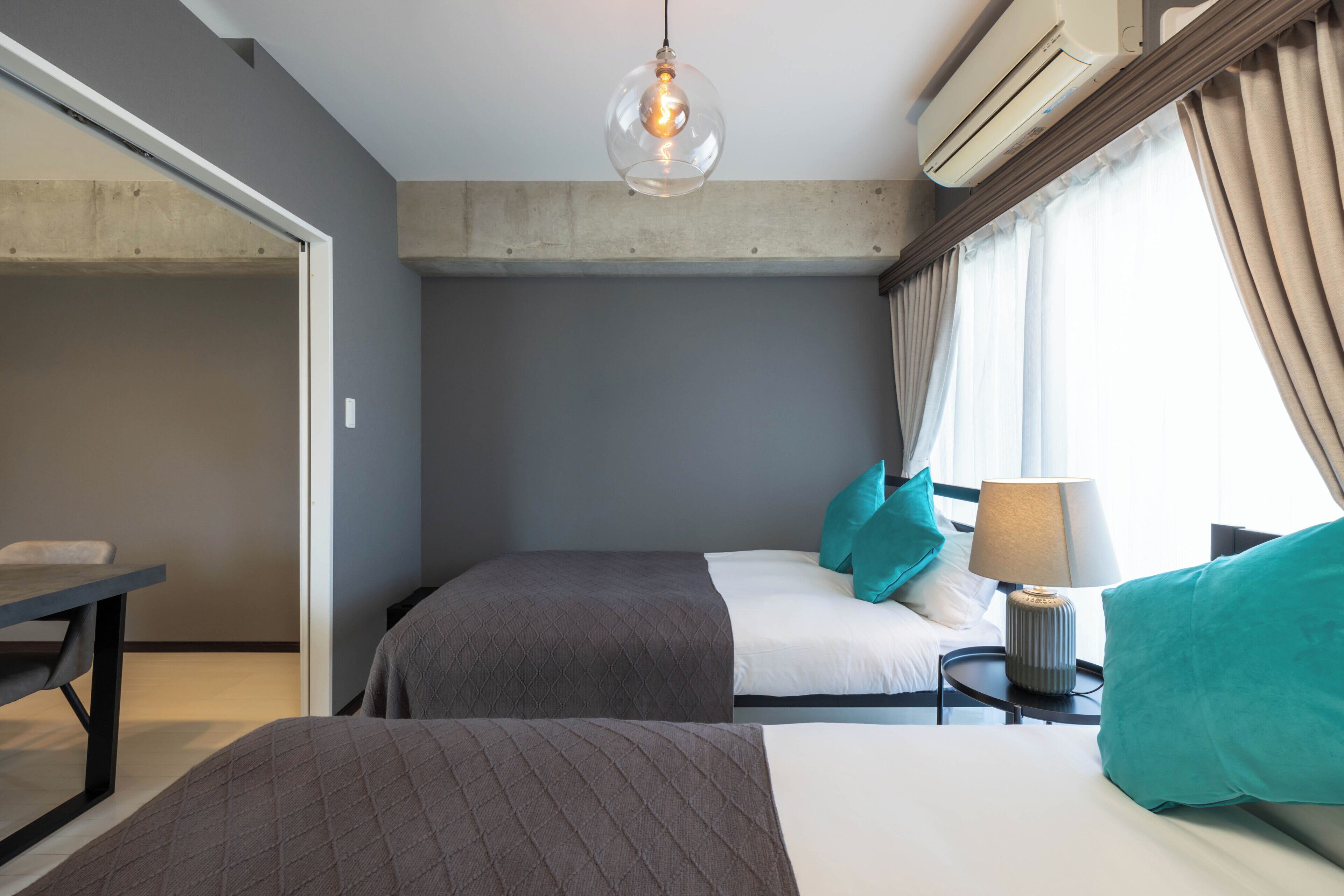 Ett hotellrum med två sängar, ett skrivbord, en lampa och ett stort fönster med gardiner.