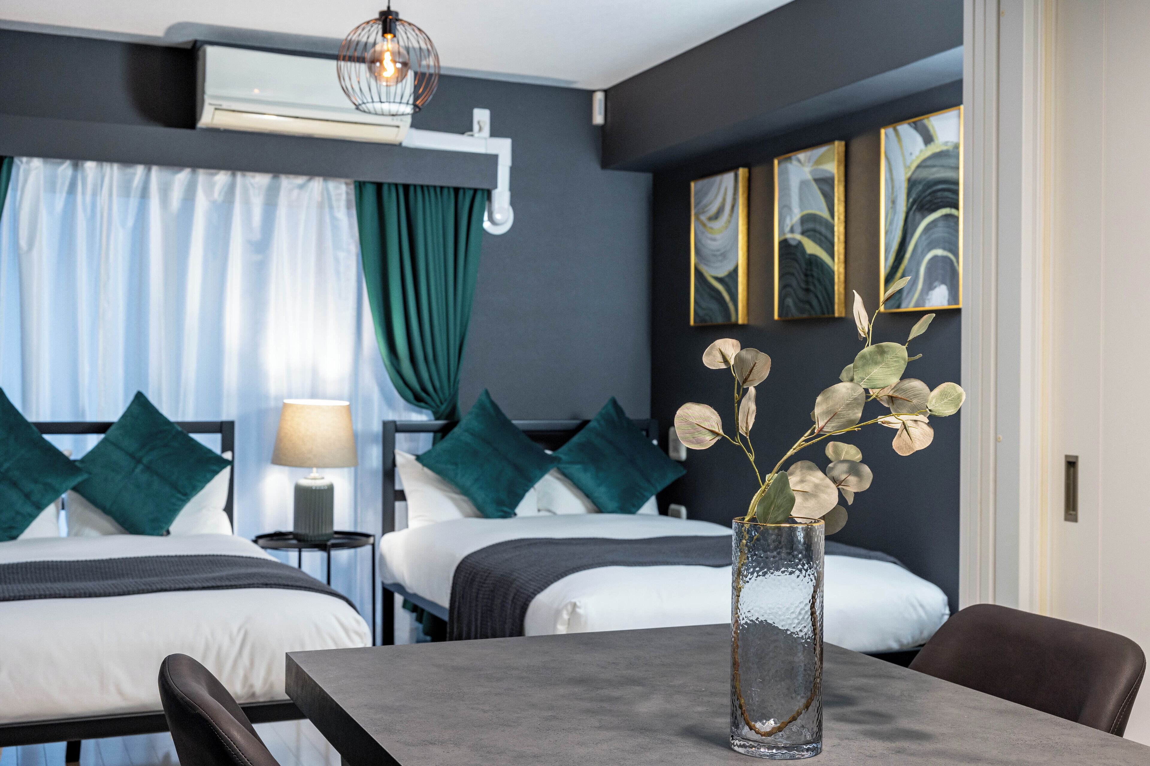Habitación de hotel con dos camas, una mesa de comedor, un jarrón con flores y cuadros en la pared.