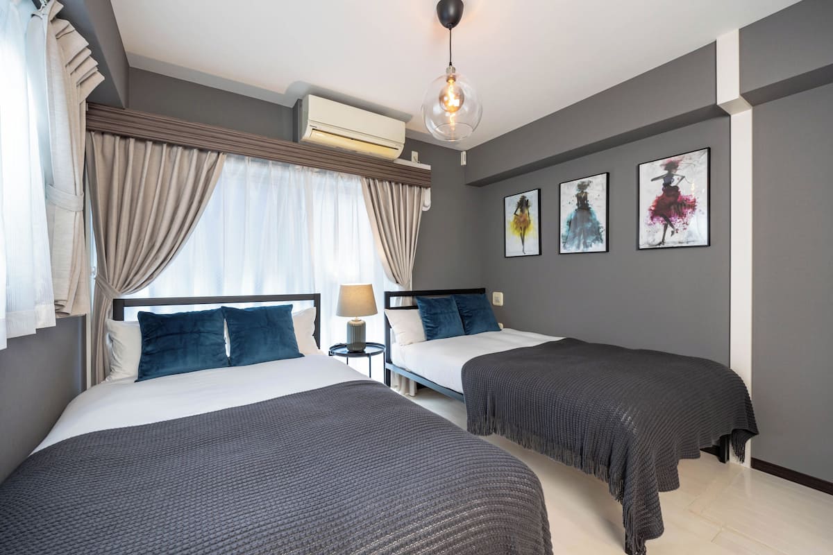 Une chambre d’hôtel avec deux lits, un ventilateur de plafond, un appareil de climatisation et des œuvres d’art encadrées accrochées au mur.