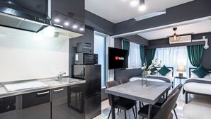 A modern kitchen with a flat-screen TV, a dining area with a table and chairs, and a living area with a sofa and a lamp. - MELL-THEATER RESORT (Osaka)