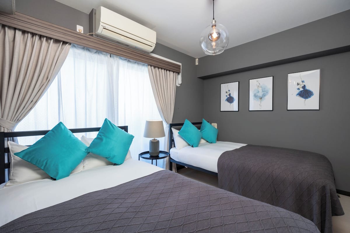 Une chambre d’hôtel avec deux lits, une table de chevet avec une lampe, un climatiseur et trois tableaux encadrés au mur.