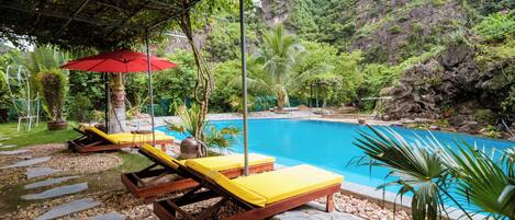 A pool area with lounge chairs and a red umbrella.
