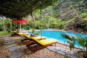 Zona de piscina con sillones de descanso y una sombrilla roja.
