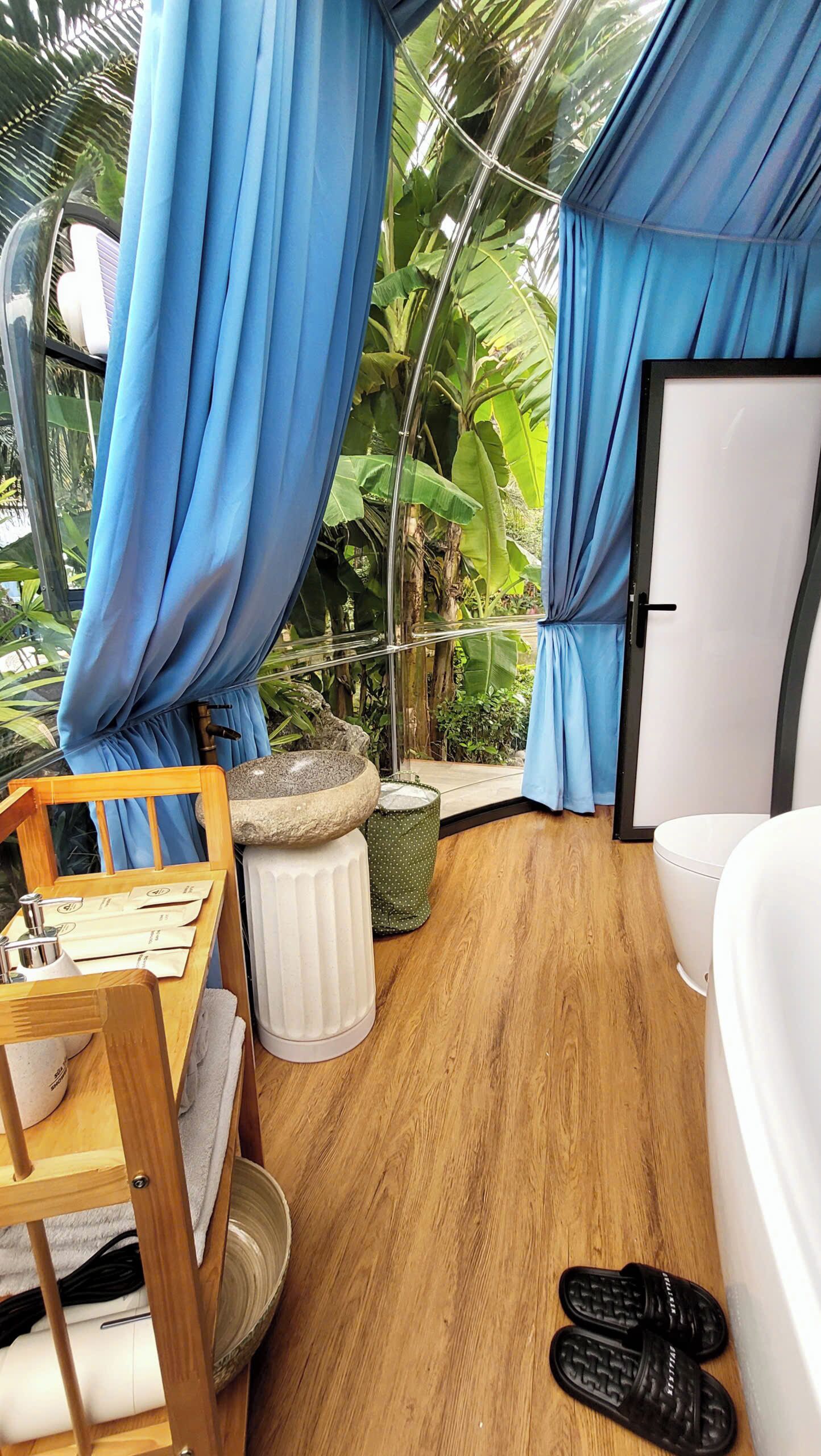A room with a wooden floor, a white sofa, a wooden chair, a stone basin, and a pair of black slippers.