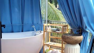 Une salle de bain avec une baignoire, une étagère en bois avec des serviettes et un lavabo en pierre.