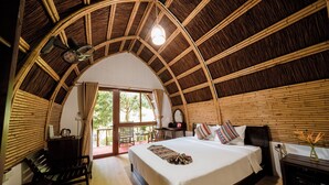 Una habitación con techo de bambú curvo, una cama con cubrecama blanco y un escritorio con lámpara.