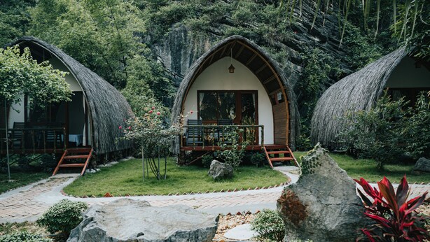 Un charmant cottage à toit de chaume, doté d’une terrasse en bois et d’un chemin de pierre menant à l’entrée.